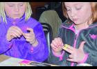 Macey Haley, right, and Addie Quade make more of their colorful rubber band bracelets  at the Eagle View Bar and Grill last Thursday night as part of a benefit event for St. Jude Children’s Research Hospital. The eight-year-olds are both 2nd Graders at Wabasha-Kellogg High School.—Photo by Michael Smith