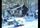 Amid this otherwise wooded and placid scene, on what would have been a beautiful but cold Wisconsin winter day, where colorful and cheerful banners fly and snow shovels rest, stands the gutted remains of the Dave and Nancy Blim house on Dry Coulee Road north of Nelson Thursday. The house burned last Wednesday afternoon, despite the best efforts of five area fire departments.—Photo by Michael Smith